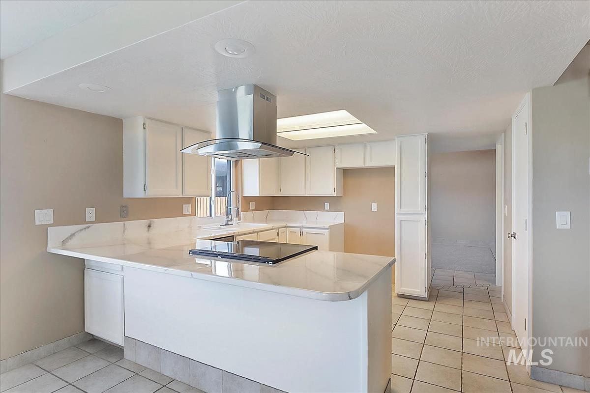 2804 West Sunrise Rim Road Boise, ID 83705 - Photo 9 of 50 Kitchen featuring a central island with an integrated cooktop, white perimeter cabinetry, and light-toned tile flooring