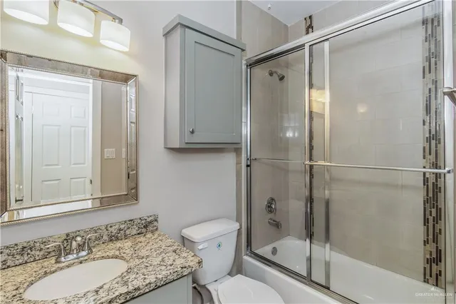 a bathroom with a granite countertop shower sink vanity and toilet