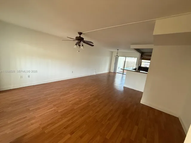an empty room with wooden floor fan and windows