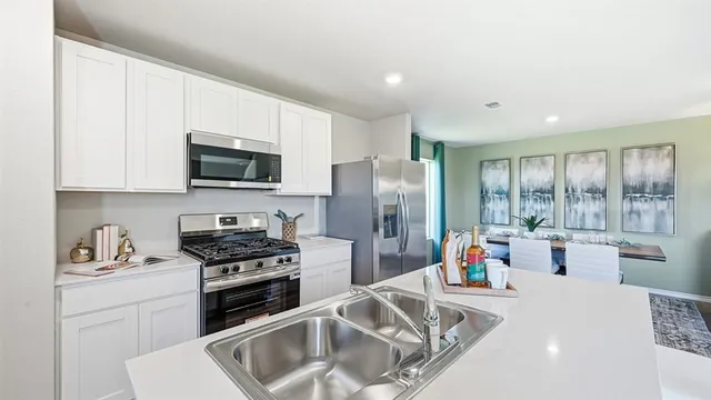 a kitchen with stainless steel appliances kitchen island granite countertop a refrigerator a stove a sink a dining table and chairs with wooden floor