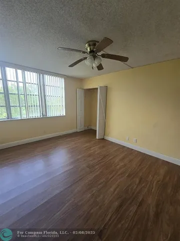 an empty room with wooden floor fan and windows