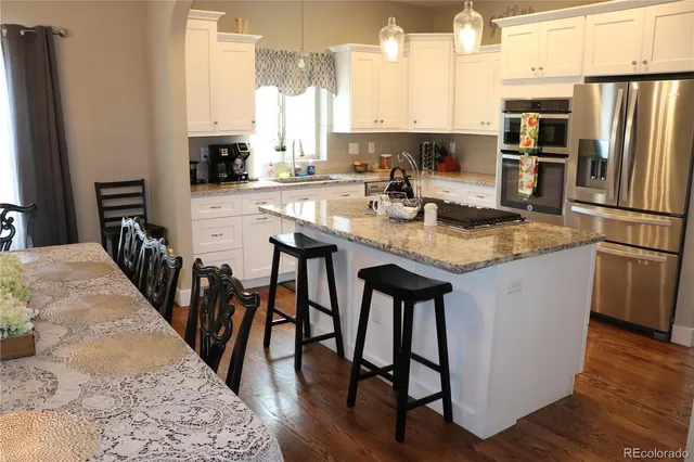 a kitchen with stainless steel appliances granite countertop a kitchen island a stove a refrigerator a sink a dining table and chairs