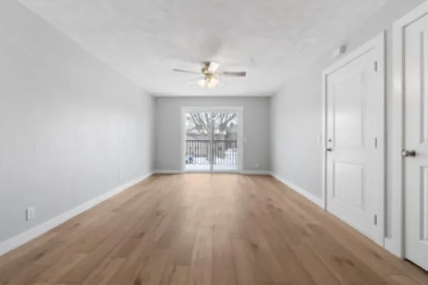 an empty room with wooden floor chandelier fan and windows