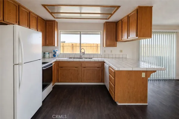 a kitchen with stainless steel appliances granite countertop a refrigerator a sink dishwasher a stove and white countertops with wooden floor