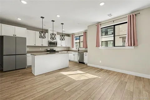 a kitchen with stainless steel appliances granite countertop a refrigerator a stove a sink and white cabinets with wooden floor next to windows