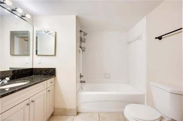 a bathroom with a granite countertop bathtub shower sink vanity and toilet