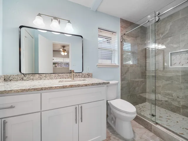a bathroom with a granite countertop sink toilet a mirror a vanity and shower