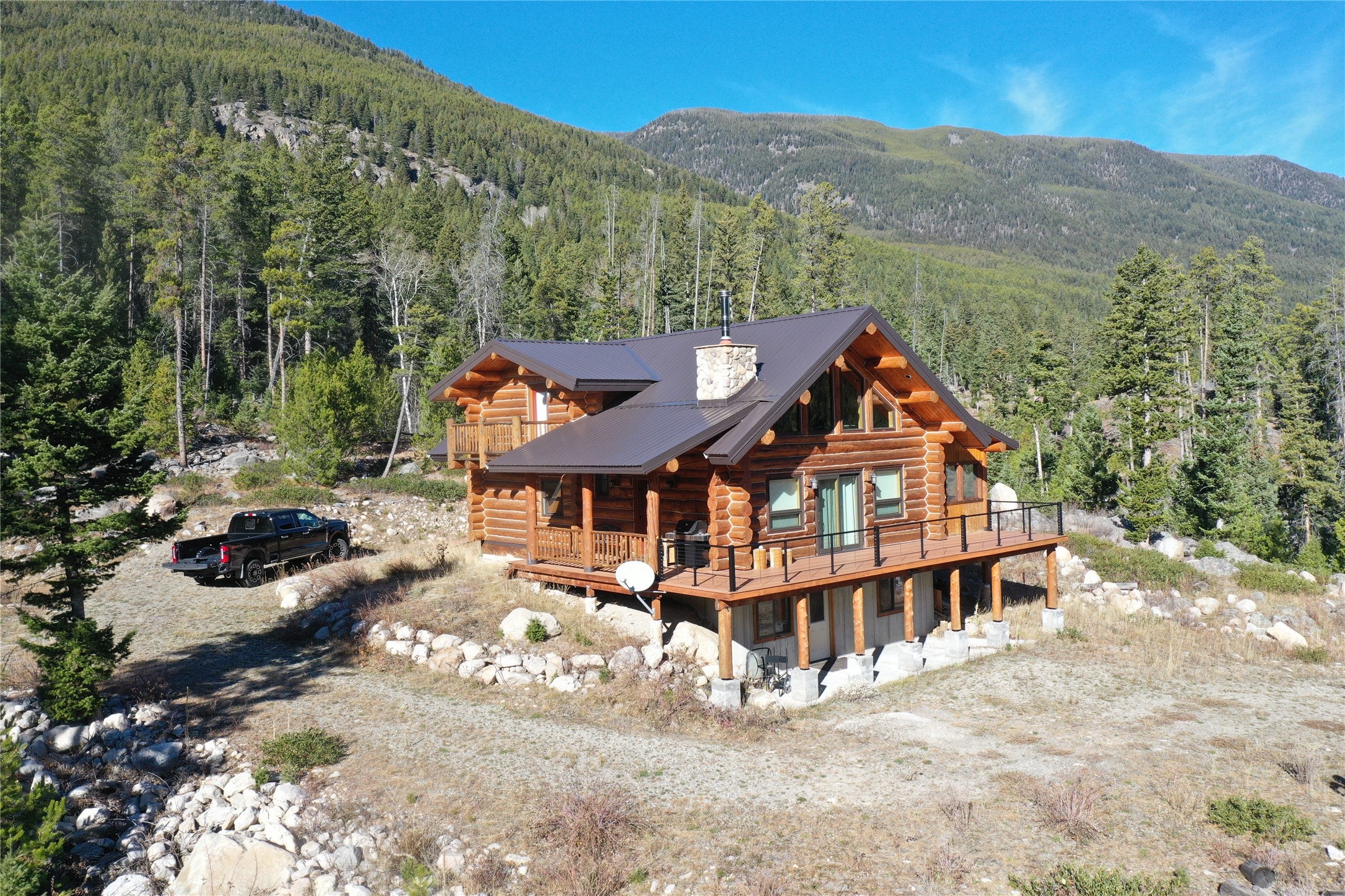 3916 Main Boulder Road McLeod, MT 59052 - Photo 20 of 38 Back of house with log siding, a deck with mountain view, a forest view, a metal roof, and driveway