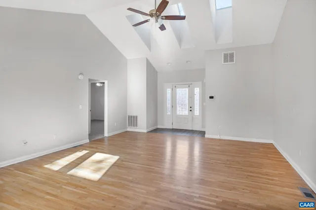 a view of an empty room with wooden floor and a ceiling fan