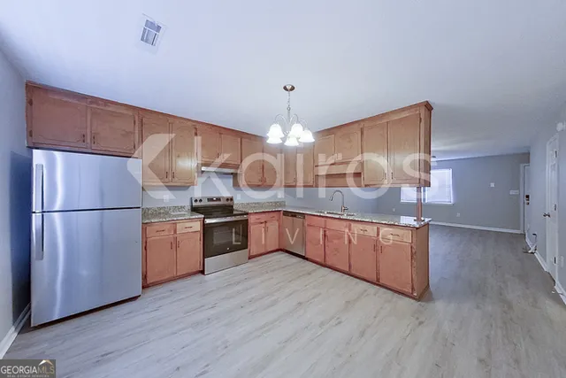 a kitchen with stainless steel appliances granite countertop a refrigerator a sink dishwasher a oven and a dining table with wooden floor