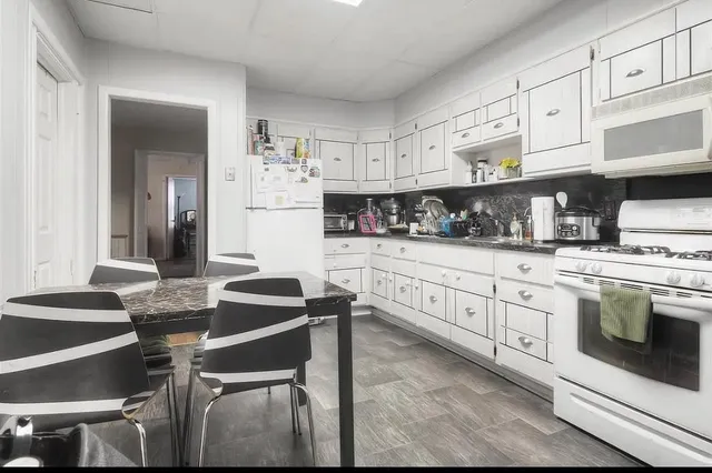 a kitchen with stainless steel appliances kitchen island granite countertop a table chairs in it and white cabinets