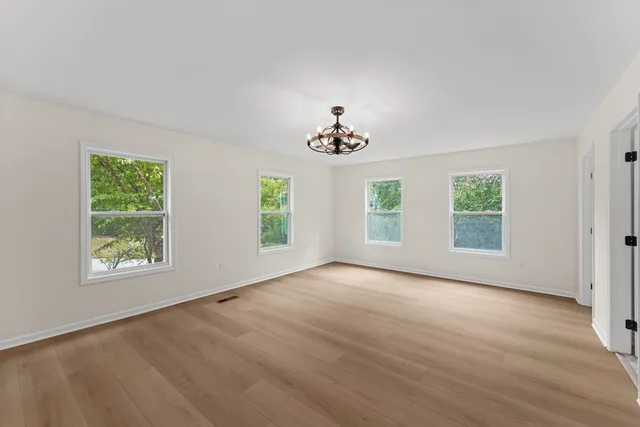 an empty room with wooden floor chandelier and windows