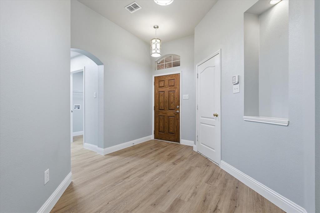 2616 Hollow Ridge Drive Denton, TX 76210 - Photo 5 of 31 Entryway featuring a wood-finish door with arched transom window, wood-finish flooring, recessed wall niche with accent lighting, and a decorative pendant light fixture