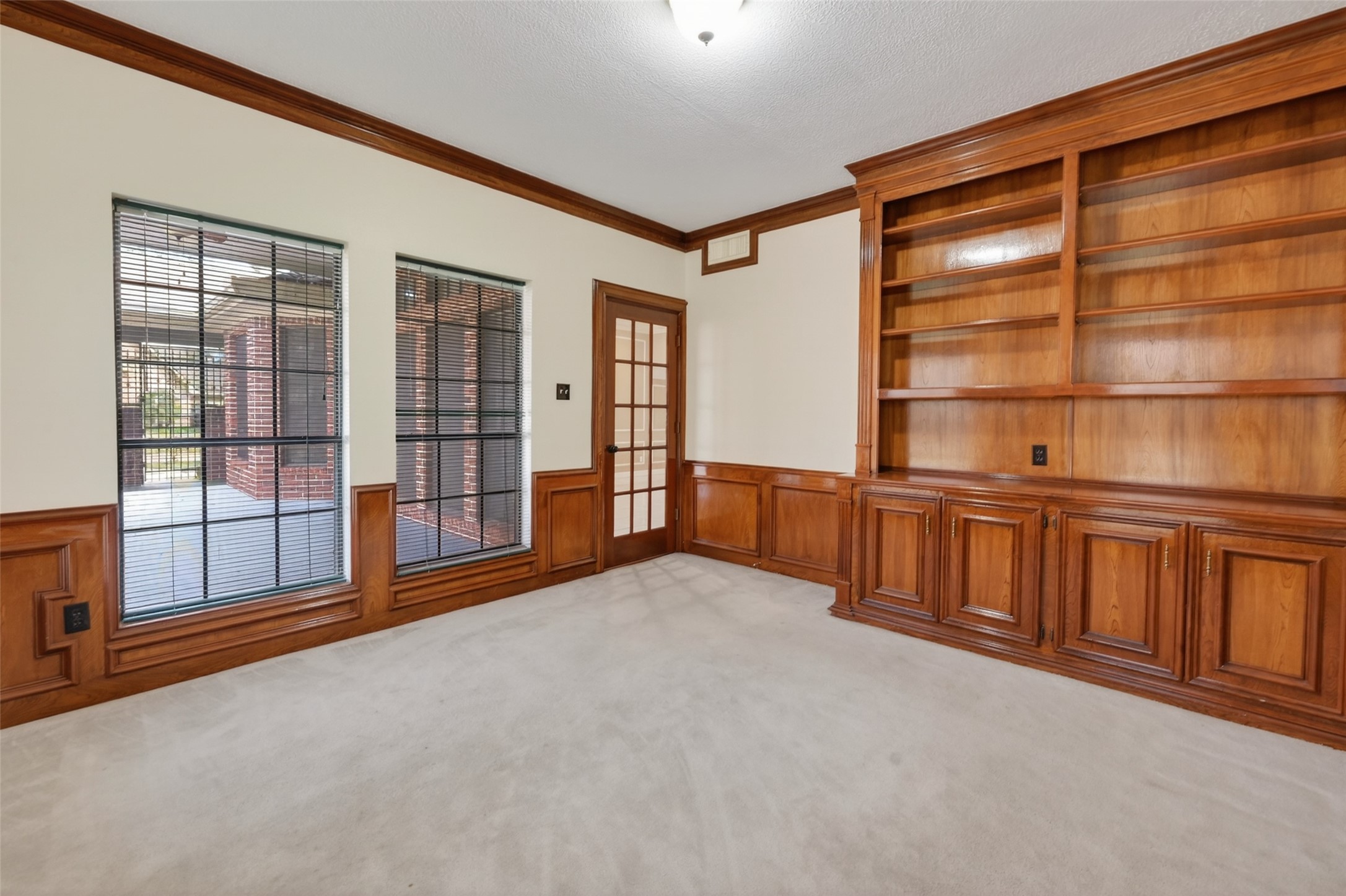 5802 Ashmere Lane Spring, TX 77379 - Photo 15 of 41 This room features a cozy, carpeted space with wooden built-in bookshelves and wainscoting. Large windows with blinds and a glass-paneled door provide natural light and outdoor views. Perfect for a home office or library.