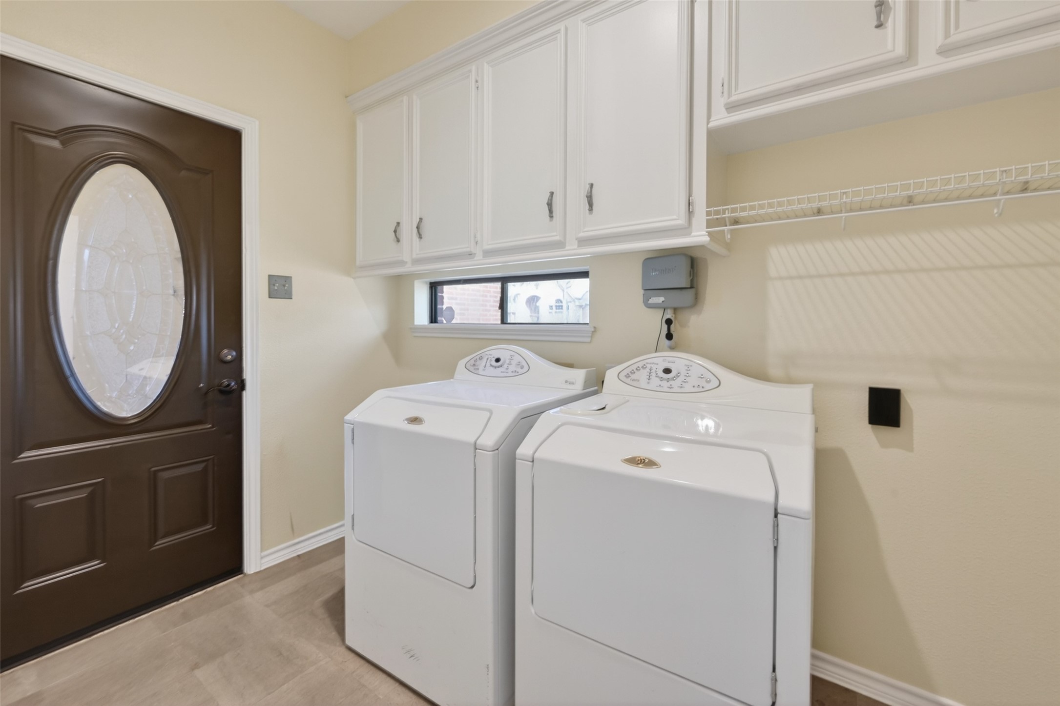 5802 Ashmere Lane Spring, TX 77379 - Photo 16 of 41 This photo shows a well-organized laundry room featuring a washer and dryer, white cabinetry for storage, a wire shelf, and an exterior door with an oval window for natural light.