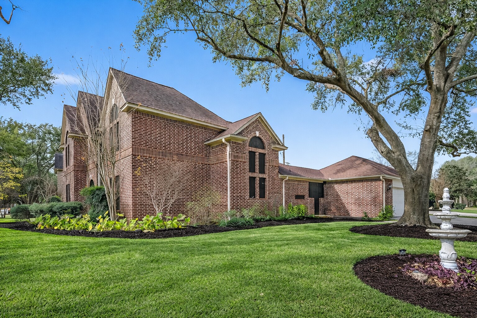 5802 Ashmere Lane Spring, TX 77379 - Photo 2 of 41 This photo showcases a charming brick home with a well-maintained lawn and mature trees. The house features a traditional design with gabled roofs and a two-story structure. A decorative fountain adds elegance to the landscaped front yard.