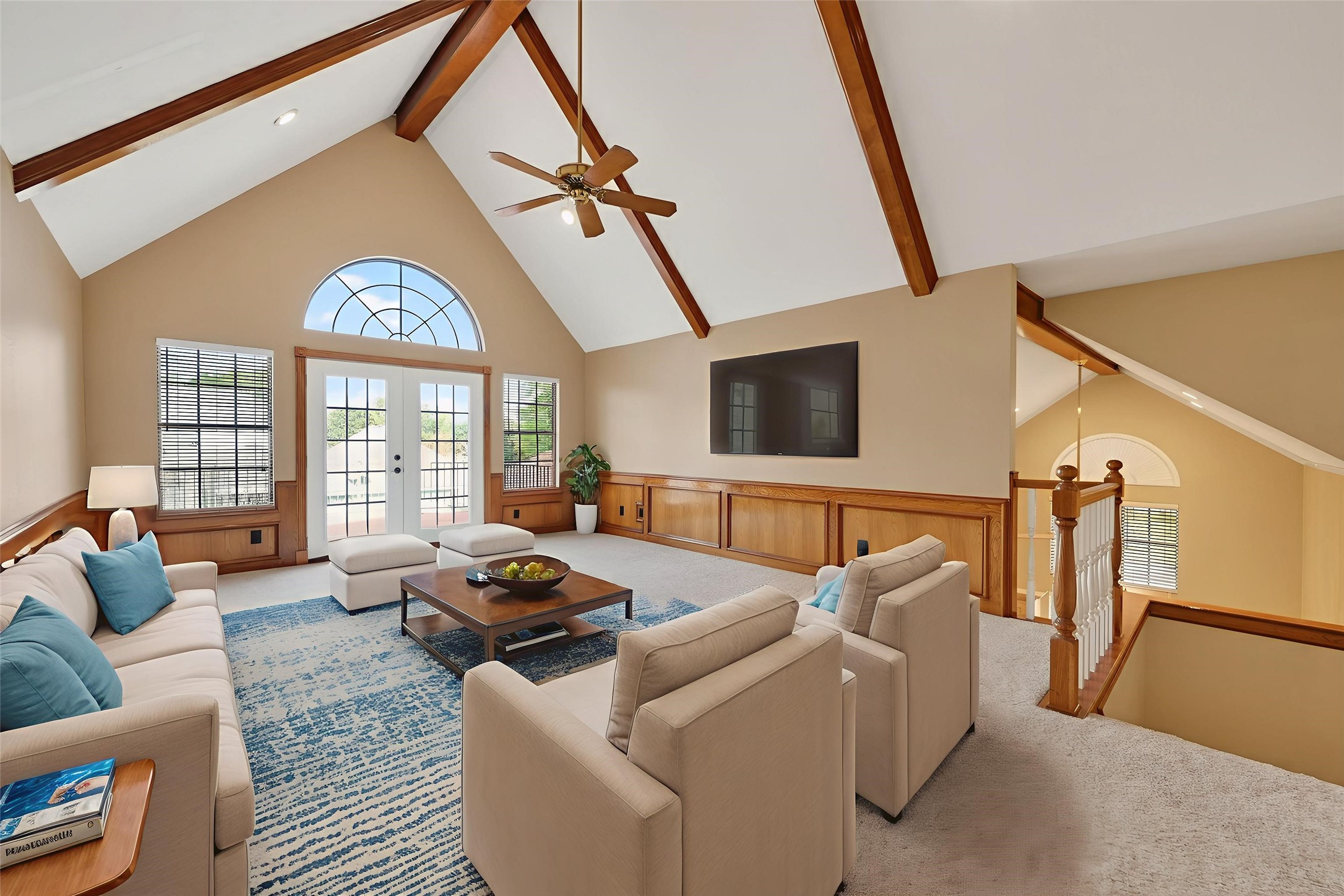 5802 Ashmere Lane Spring, TX 77379 - Photo 21 of 41 This spacious living room features high vaulted ceilings with wooden beams, a large arched window for natural light, and a cozy seating area with plush sofas. The room is accented with wood paneling and has a modern fireplace, offering a warm and inviting atmosphere.