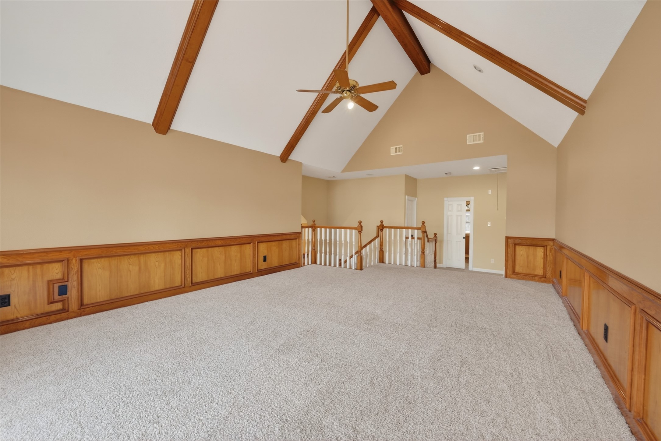 5802 Ashmere Lane Spring, TX 77379 - Photo 22 of 41 This spacious room features high vaulted ceilings with exposed wooden beams, neutral walls, and plush carpeting. A ceiling fan is centrally positioned, and the room is accented with wooden wainscoting. It has an open layout with a view into an adjacent area through a railing.