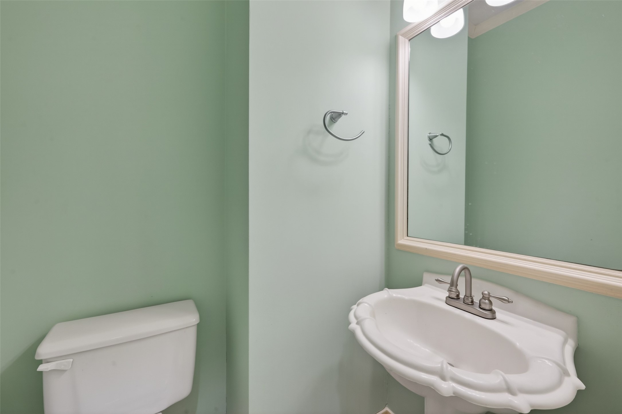 5802 Ashmere Lane Spring, TX 77379 - Photo 23 of 41 This bathroom features a soft green color scheme with a classic pedestal sink, a large framed mirror, and a toilet. The space is simple and elegant, offering a fresh, clean look.