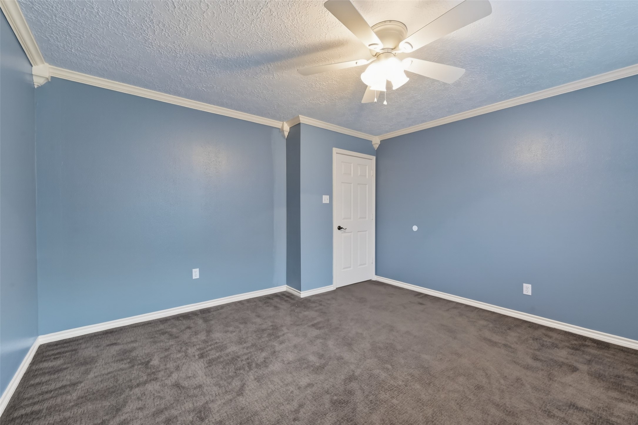 5802 Ashmere Lane Spring, TX 77379 - Photo 25 of 41 This room features soft blue walls with elegant white crown molding and trim. It has a ceiling fan for comfort, plush dark carpet, and ample natural light, creating a cozy and inviting space.