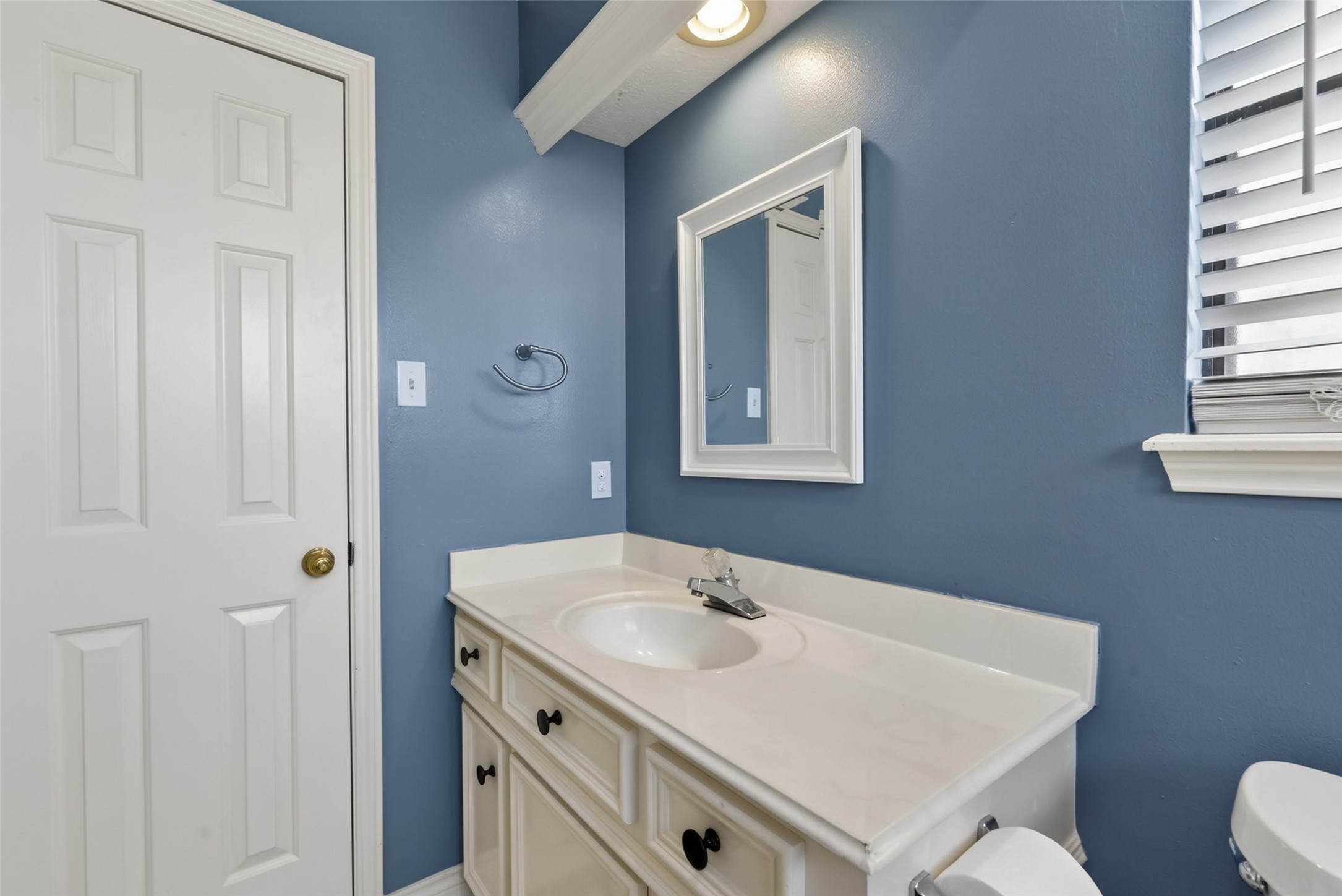5802 Ashmere Lane Spring, TX 77379 - Photo 26 of 41 Charming bathroom with blue walls and white accents. Features a single vanity with storage, a mirror, and a window with blinds for natural light.