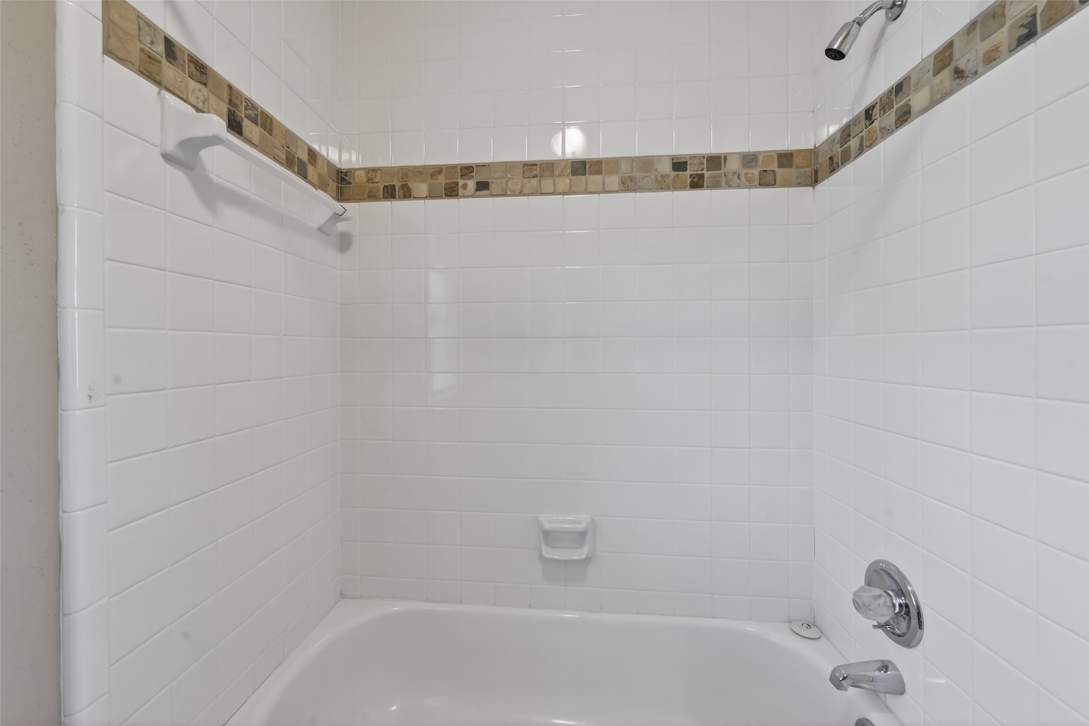 5802 Ashmere Lane Spring, TX 77379 - Photo 30 of 41 This photo shows a clean, modern bathroom with a white tiled shower and bathtub. It features a decorative tile border and a convenient built-in soap holder, providing a fresh and simple look.