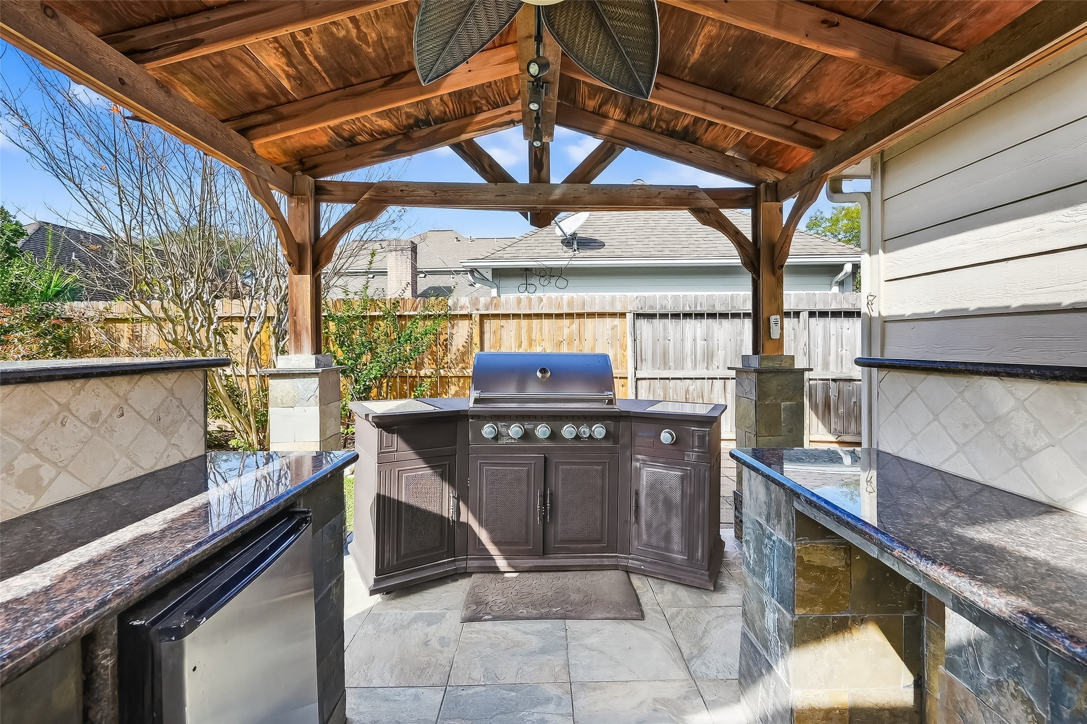 5802 Ashmere Lane Spring, TX 77379 - Photo 37 of 41 This photo showcases a stylish outdoor kitchen with a covered wooden pergola, featuring a built-in grill and ample counter space, perfect for backyard entertaining.