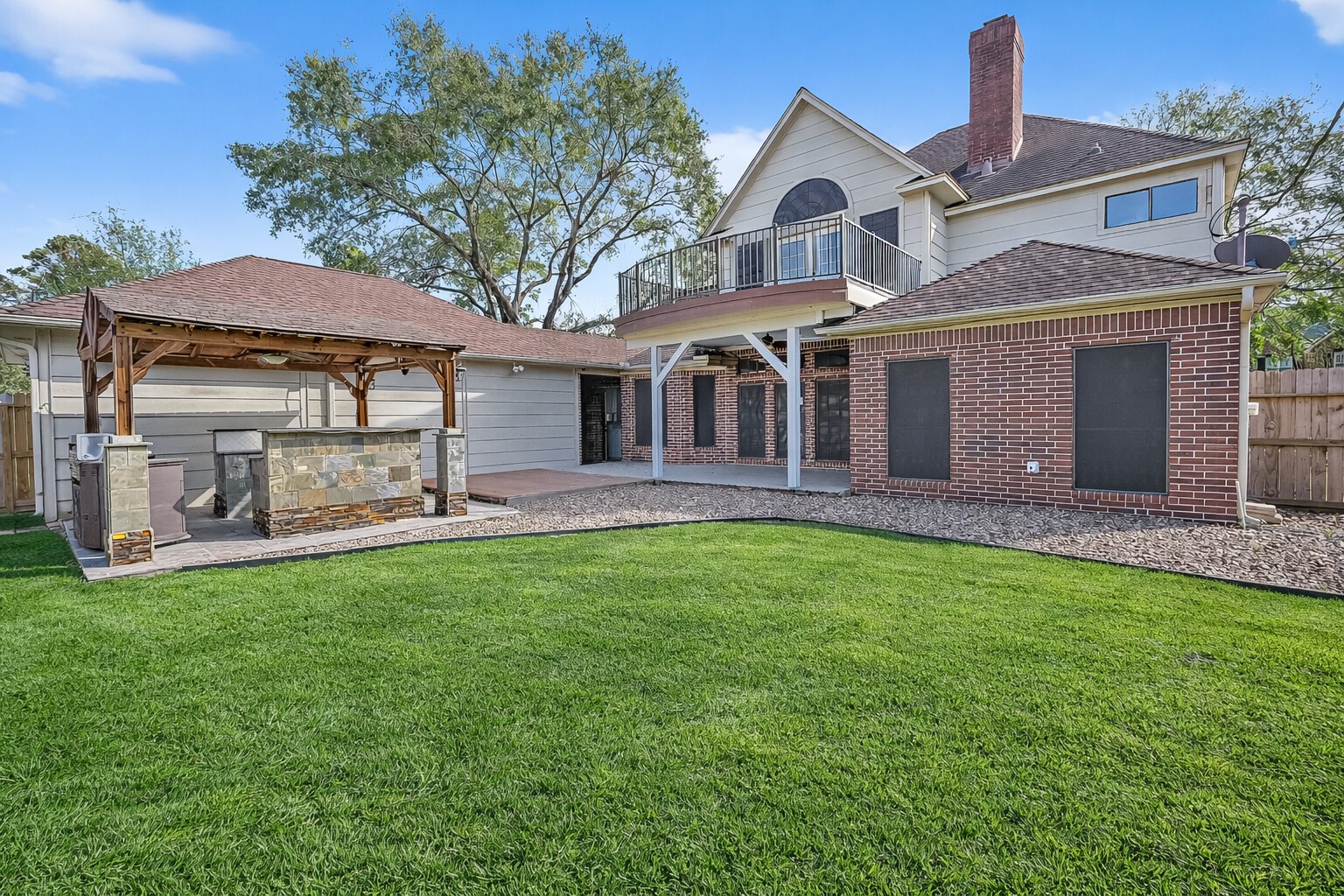 5802 Ashmere Lane Spring, TX 77379 - Photo 40 of 41 This photo showcases a spacious backyard with a well-maintained lawn, a large brick and siding house featuring a balcony, and a covered outdoor kitchen area perfect for entertaining.