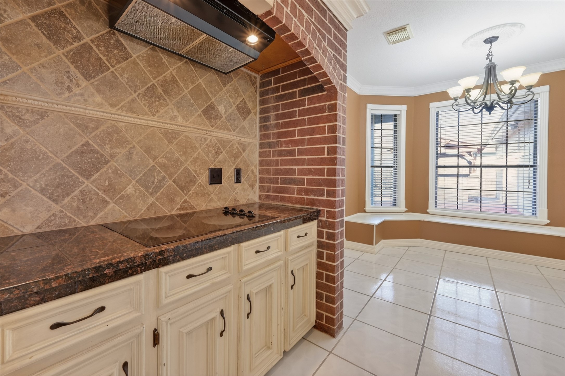 5802 Ashmere Lane Spring, TX 77379 - Photo 9 of 41 This kitchen features a cozy nook with large windows and a chandelier, offering plenty of natural light. It has a stylish brick and tile backsplash, with a sleek cooktop and elegant cabinetry, creating a warm and inviting space.