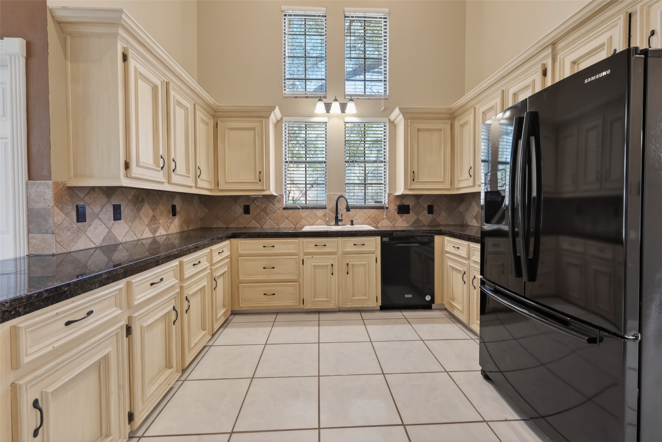 5802 Ashmere Lane Spring, TX 77379 - Photo 10 of 41 This kitchen features high ceilings and abundant natural light from tall windows. It has cream-colored cabinetry, dark countertops, tile backsplash, and modern black appliances, providing a spacious and elegant cooking area.