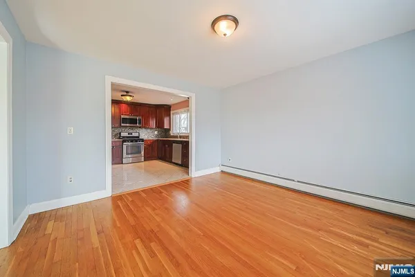 a view of empty room with wooden floor and kitchen