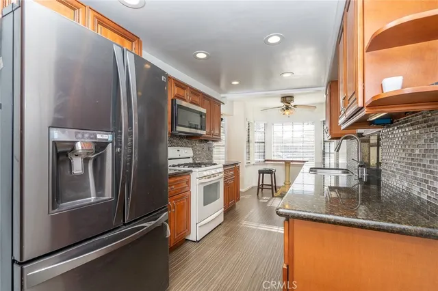 a kitchen with stainless steel appliances granite countertop a refrigerator a stove and a sink with wooden floor