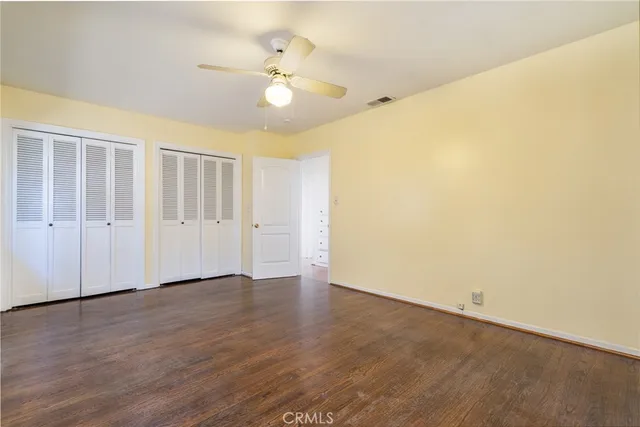 an empty room with wooden floor and fan