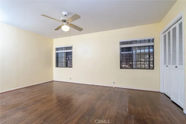 an empty room with wooden floor chandelier fan and windows
