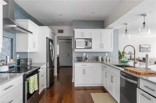 a kitchen with stainless steel appliances granite countertop a refrigerator a stove a sink dishwasher and white cabinets with wooden floor