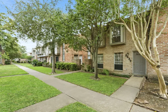 a view of a white house next to a yard with big trees