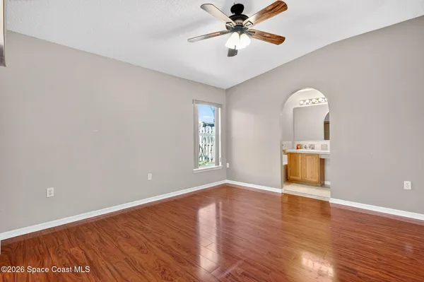 an empty room with wooden floor chandelier fan and windows