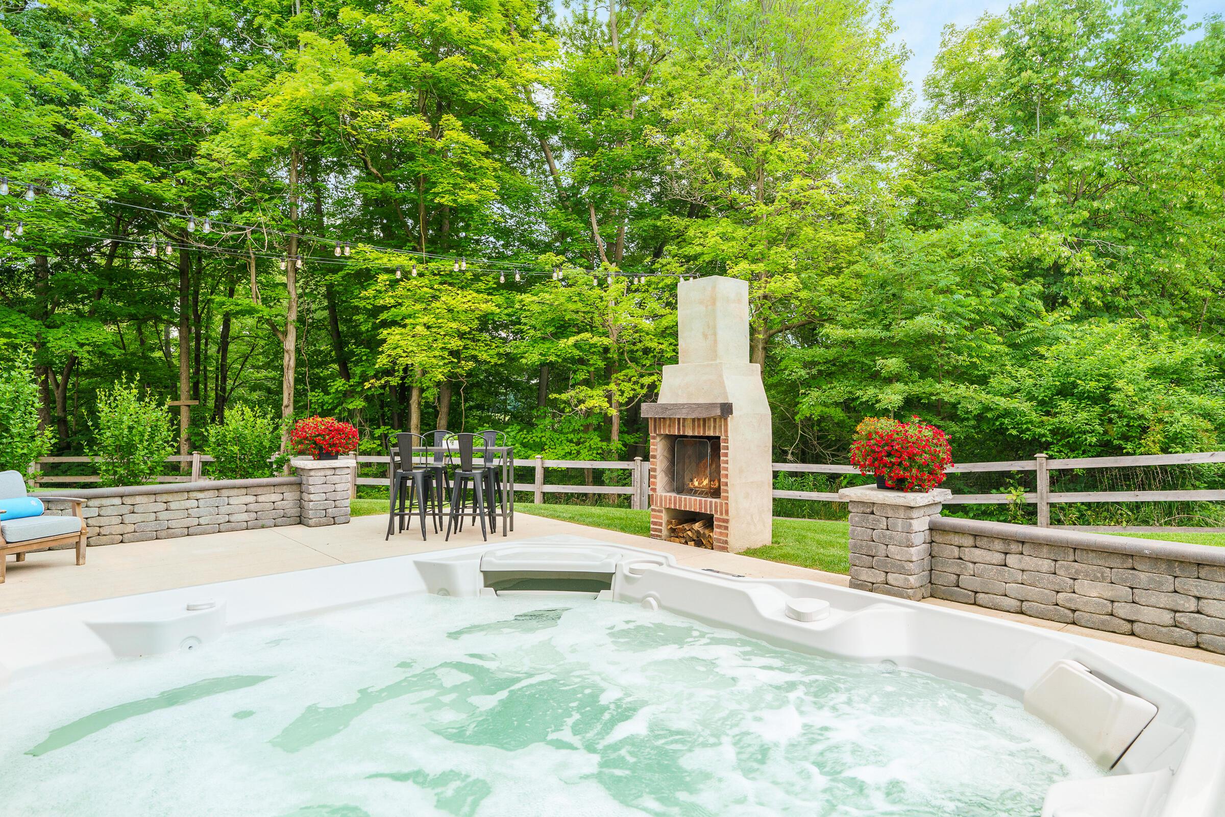 The decadent paver patio, features a generous hot tub, wood burning fireplace and space to entertain like a King with wooded views.