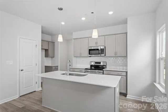 a kitchen with stainless steel appliances a sink stove refrigerator and white cabinets with wooden floor