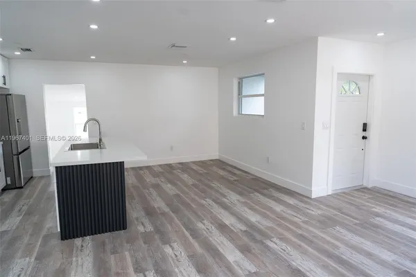 an empty room with wooden floor and kitchen view