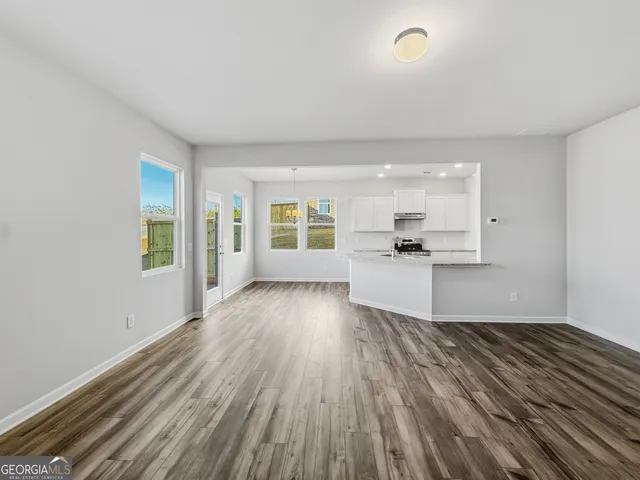 a view of empty room with wooden floor and kitchen view