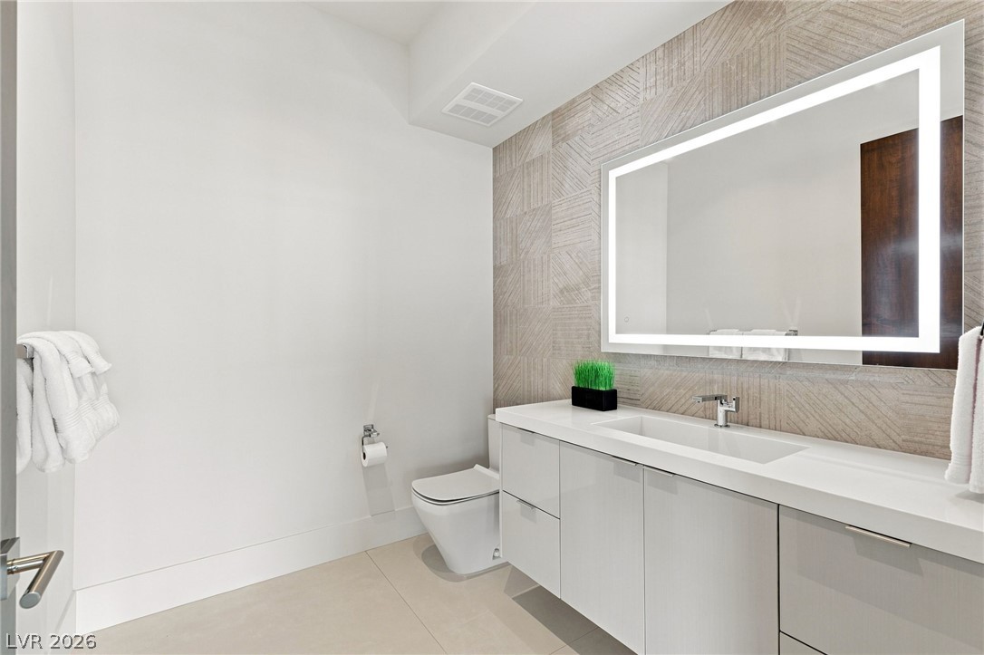 677 Overlook Rim Drive Henderson, NV 89012 - Photo 52 of 97 Textured tile backdrops a modern floating vanity with an integrated sink and illuminated mirror.
