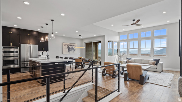 355 East Overlook Loop Hideout, UT 84036 - Photo 5 of 40 Open-concept living space with wood-finish flooring, a contemporary kitchen featuring dark cabinetry and stainless steel appliances, a center island with seating, a dining area, and a living room with a prominent wall of windows