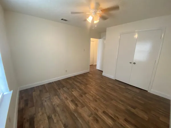an empty room with wooden floor closet and fan