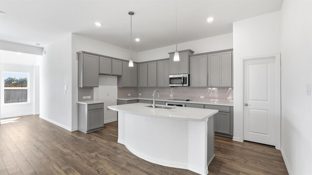 2529 Rivers W Road Anna, TX 75409 - Photo 18 of 40 Modern kitchen featuring a curved island with integrated sink, stainless steel appliances, grey cabinetry, light-toned countertops, and wood-finish flooring