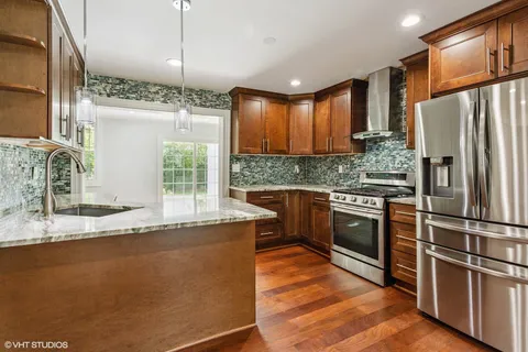 a kitchen with stainless steel appliances granite countertop a refrigerator a stove and a sink with wooden floors