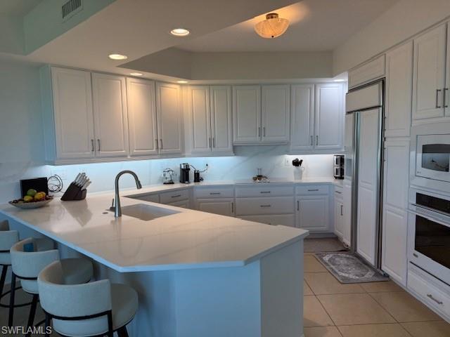 295 Grande Way, Unit 505 Naples, FL 34110 - Photo 2 of 20 Kitchen featuring a peninsula, white cabinetry, light tile patterned floors, white oven, and paneled built in refrigerator