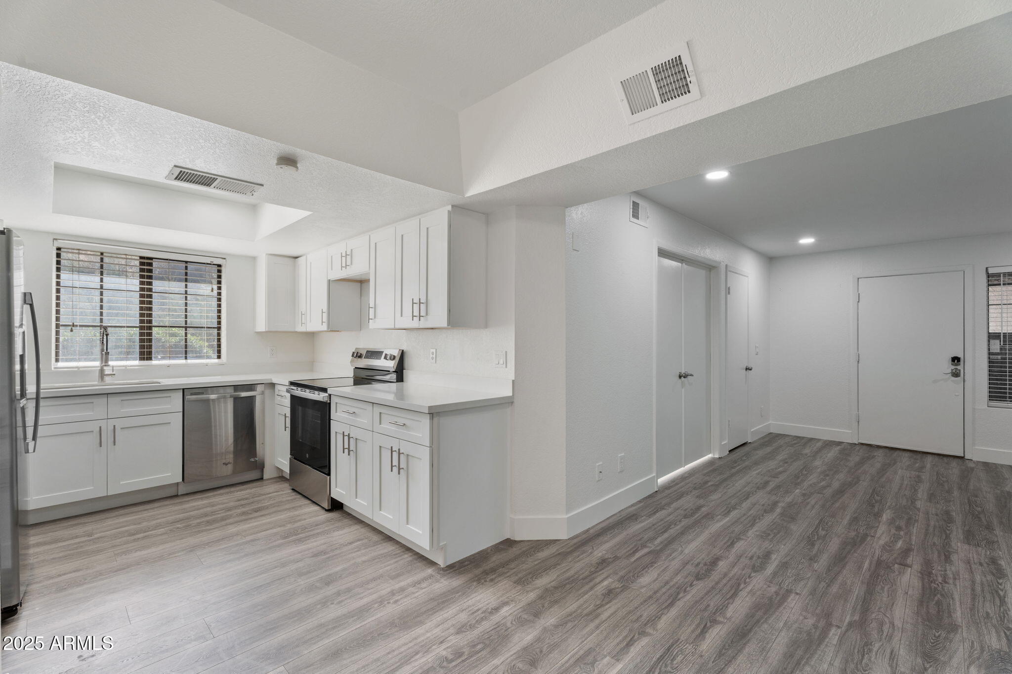 1905 East University Drive, Unit 133 Tempe, AZ 85288 - Photo 20 of 38 a large white kitchen with a refrigerator a sink dishwasher a stove and white cabinets with wooden floor