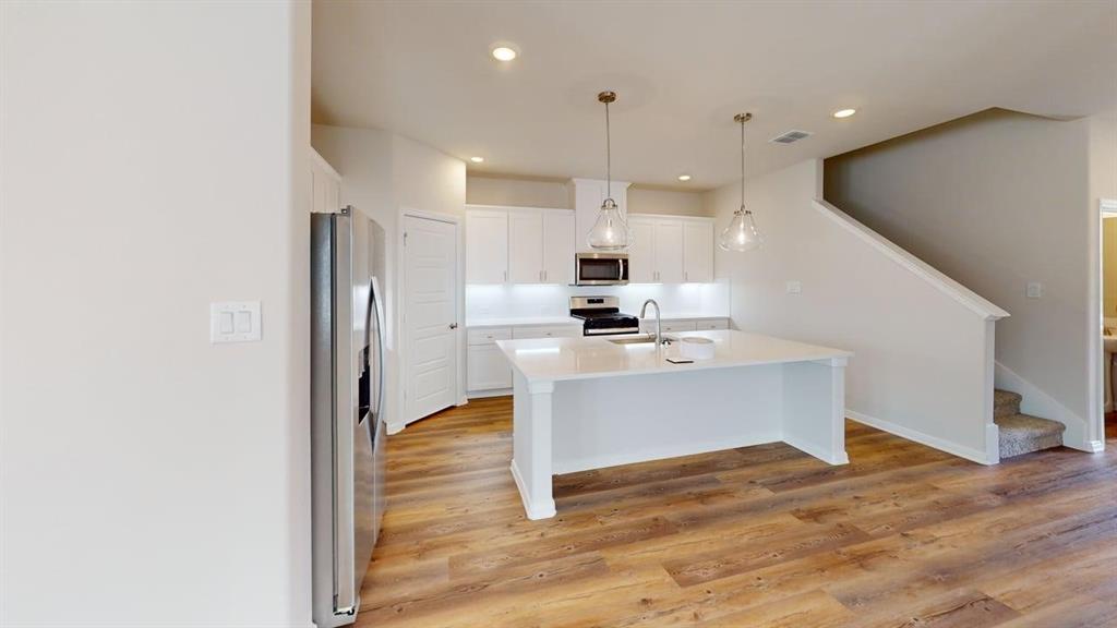 1840 Rosedale Avenue Van Alstyne, TX 75495 - Photo 5 of 24 Modern kitchen featuring white cabinetry, a large center island with a sink, stainless steel appliances, and wood-finish flooring