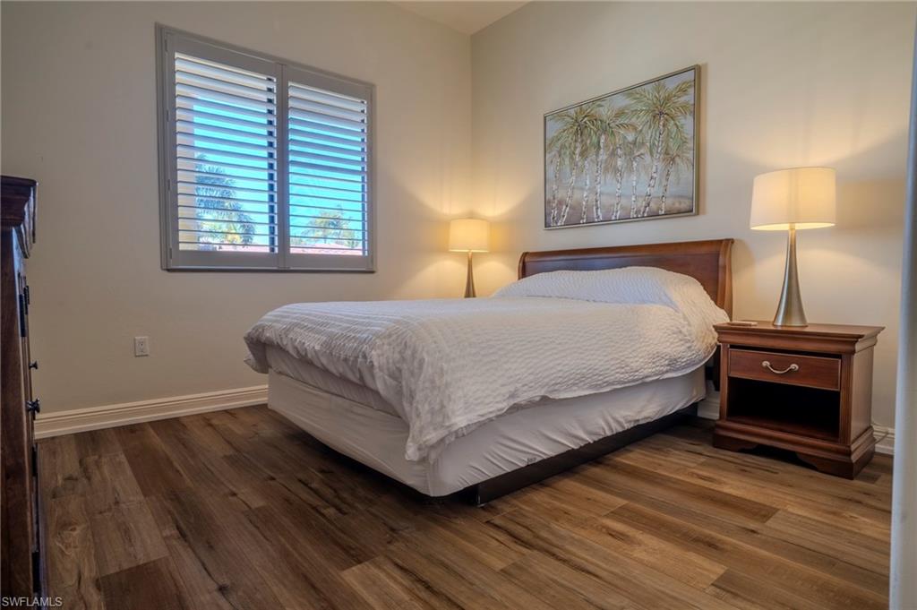 1045 Sandpiper Street, Unit G204 Naples, FL 34102 - Photo 21 of 40 a bedroom with a bed and a lamp on wooden floor